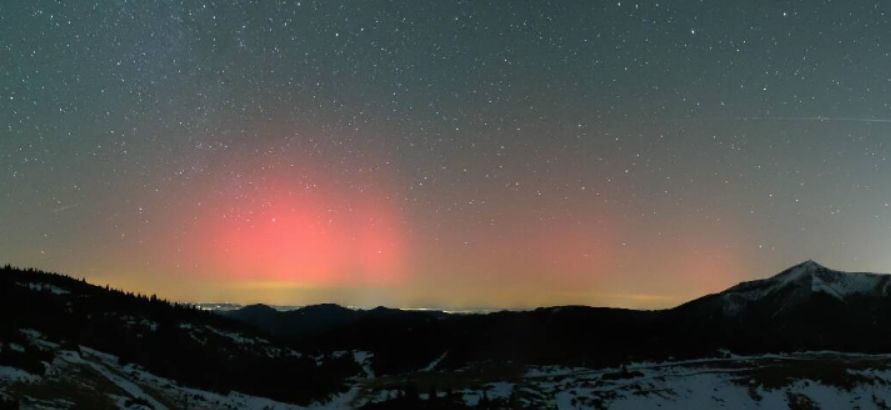 Sternenhimmel mit roten Aurora-Strahlen. Im Vordergrund verschneite Berglandschaft.
