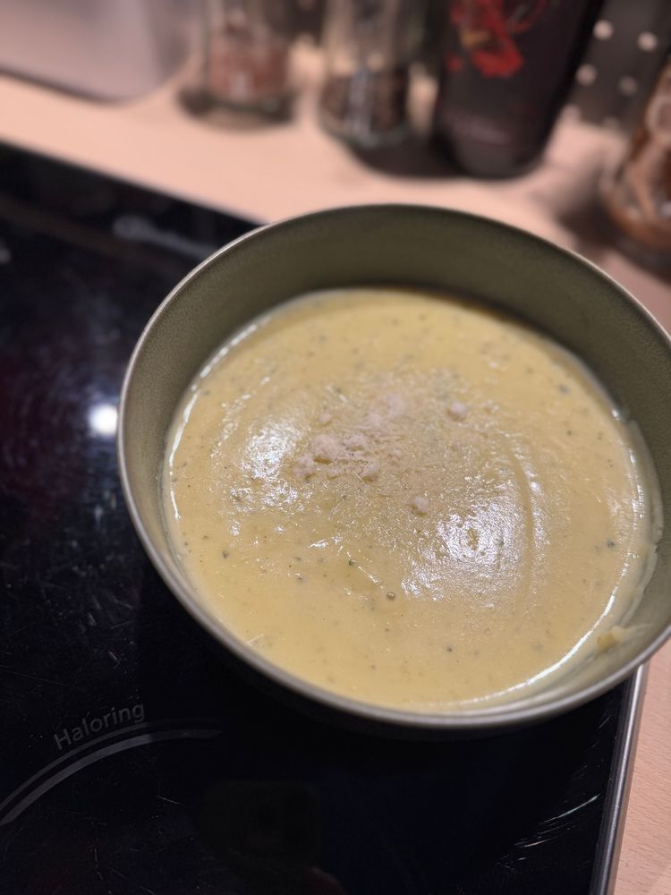 Nahaufnahme einer salbeifarbenen Bowl mit pürierter Kartoffel-Zucchini-Suppe mit Parmesan als Topping.