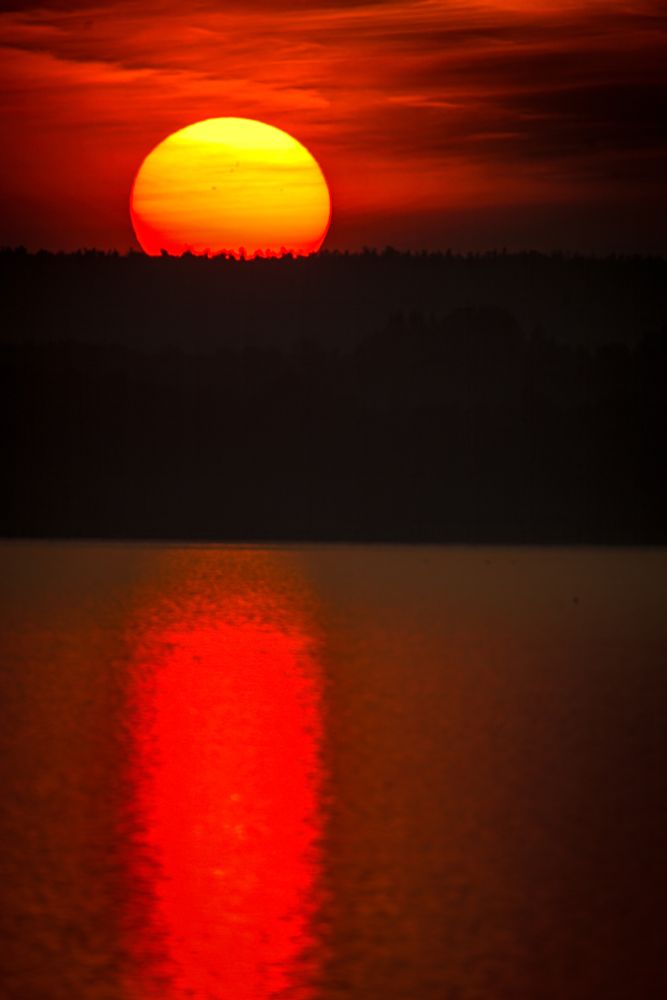 Image of large bright red sun dawning over a body of water.