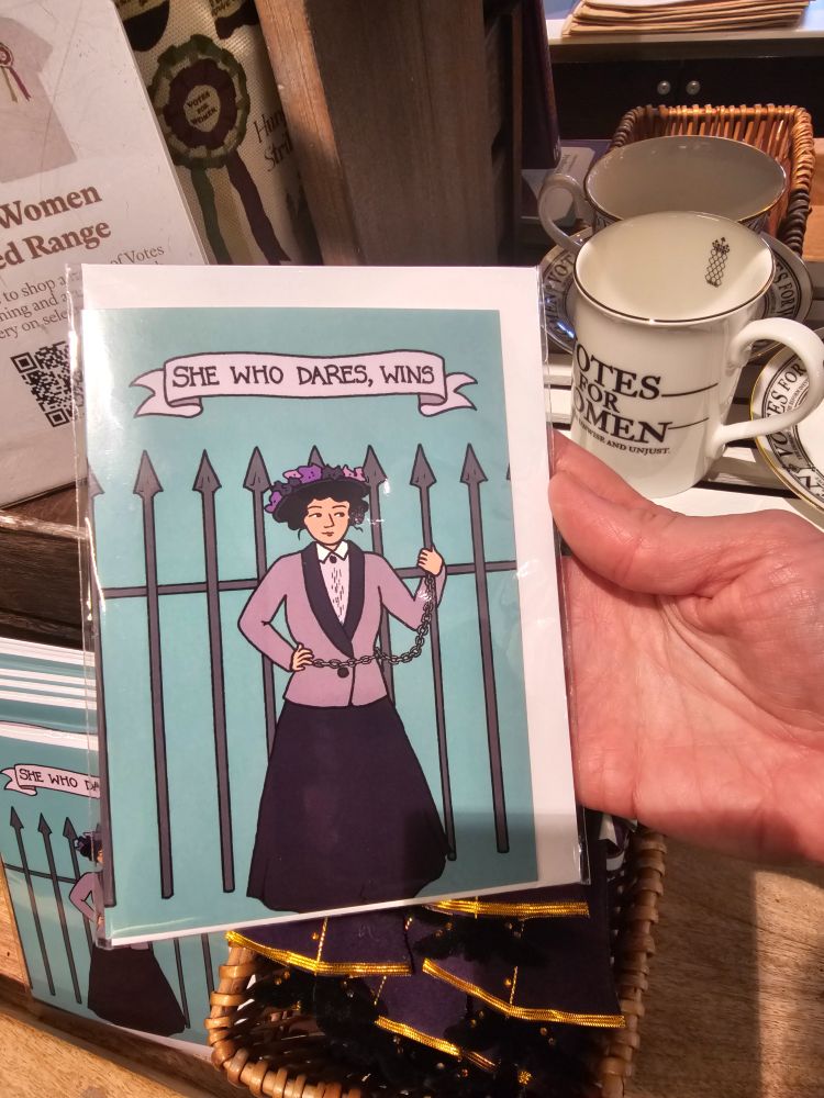 A greeting card with an illustration of a woman chained to a railing, with the words 'She who dares, wins'
