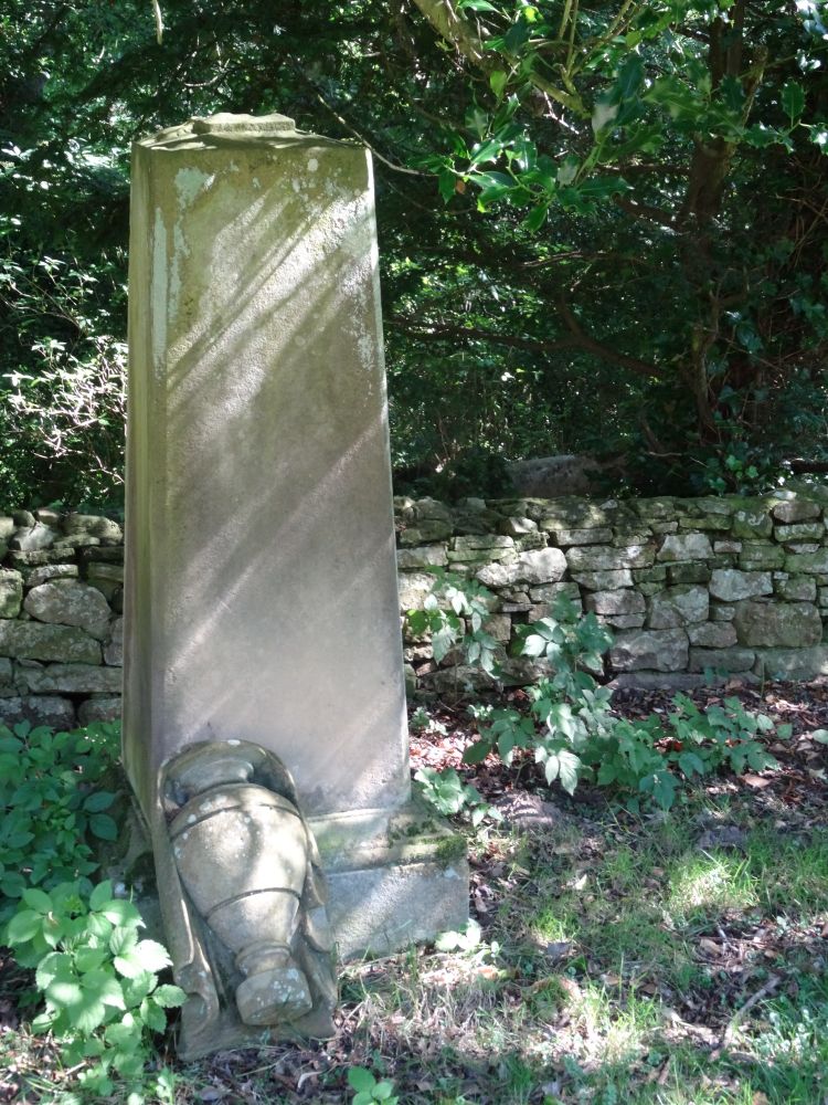 Sandstone monument in the form of a square pillar with urn. The urn has fallen (or been removed) and now rests against the base, still in one piece. The sandstone has weathered so badly that there are only the slightest traces to suggest that the front face ever had an inscription.