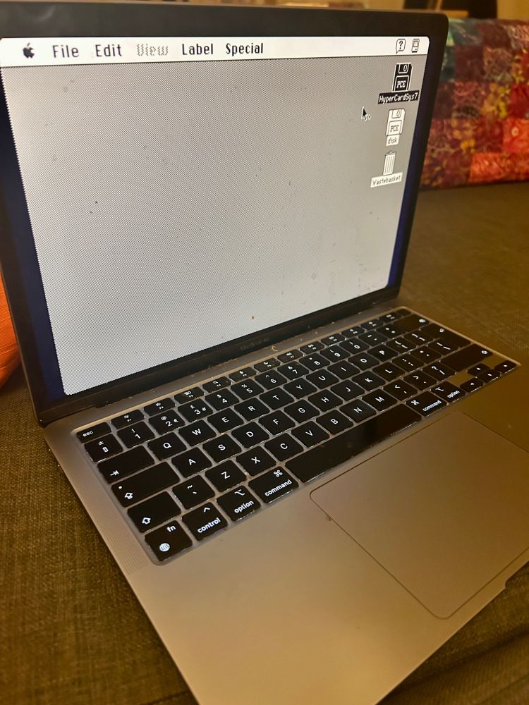 A modern 2022 silver MacBook Air device (apparently) running the original 1984 Mac OS  - taskbar with black on grey text, the Apple symbol, then File / Edit / View 