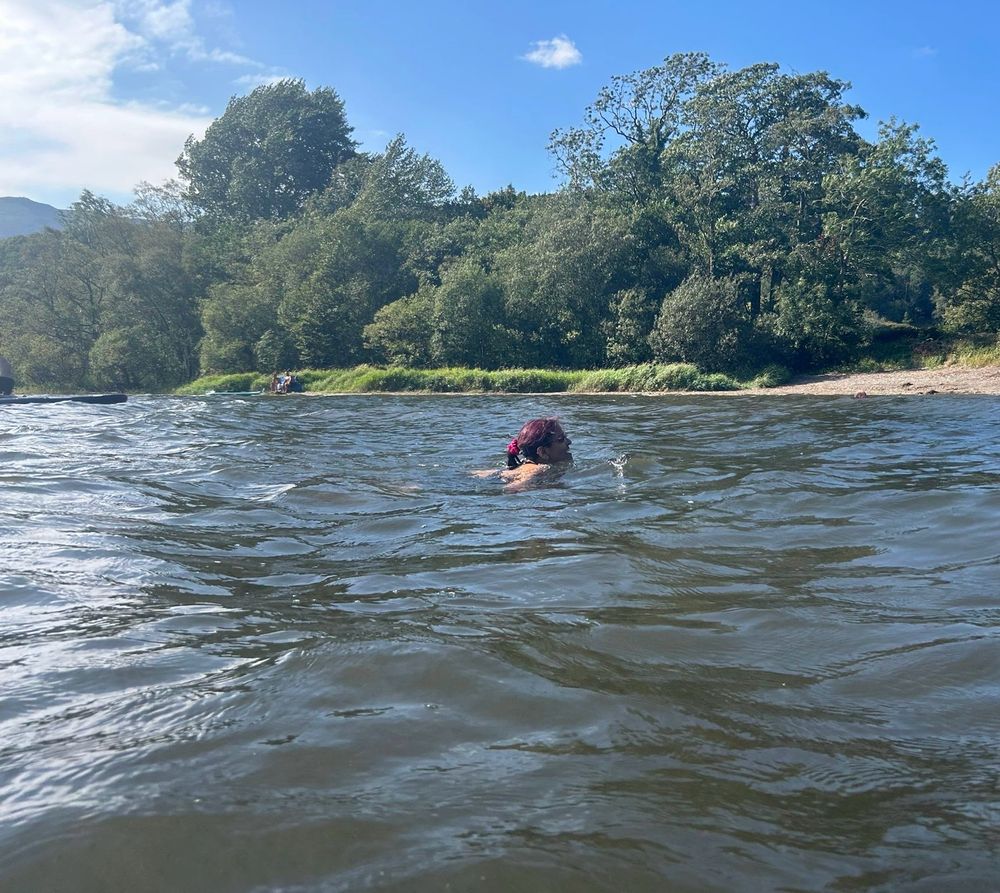 A swimmer with brown skin and pinkish red hair (me) swimming at the sunlit lake surface 