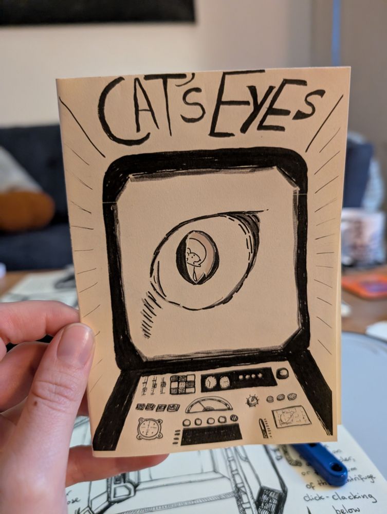 The front cover of a cream and black coloured zine called Cat's Eyes. It features a screen with a control panel beneath it. On the screen is a cat's eye with the centre of the pupil cut out. Through the cut-out, you can see a mouse wearing an astronaut helmet 