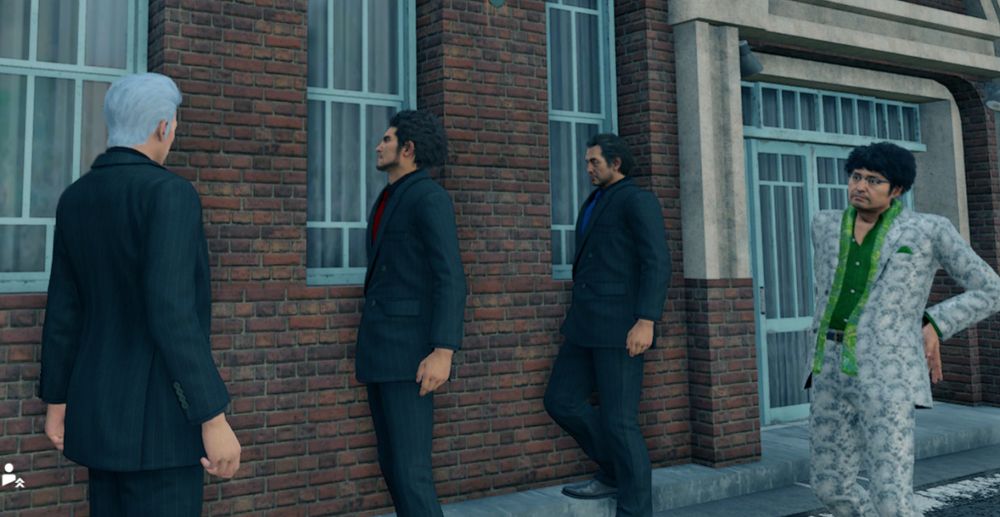 Screenshot from Yakuza: Like a Dragon. Four men in suits in front of a brick building. The three on the left (Joongi, Kasuga, Adachi) are wearing navy blue suits and ties, the one on the right (Nanba) is wearing a leisure suit. 