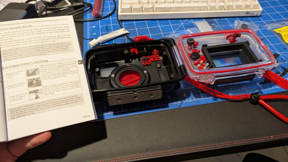 An underwater camera housing and an instruction booklet explaining how to apply silicone grease to the housing's o-ring