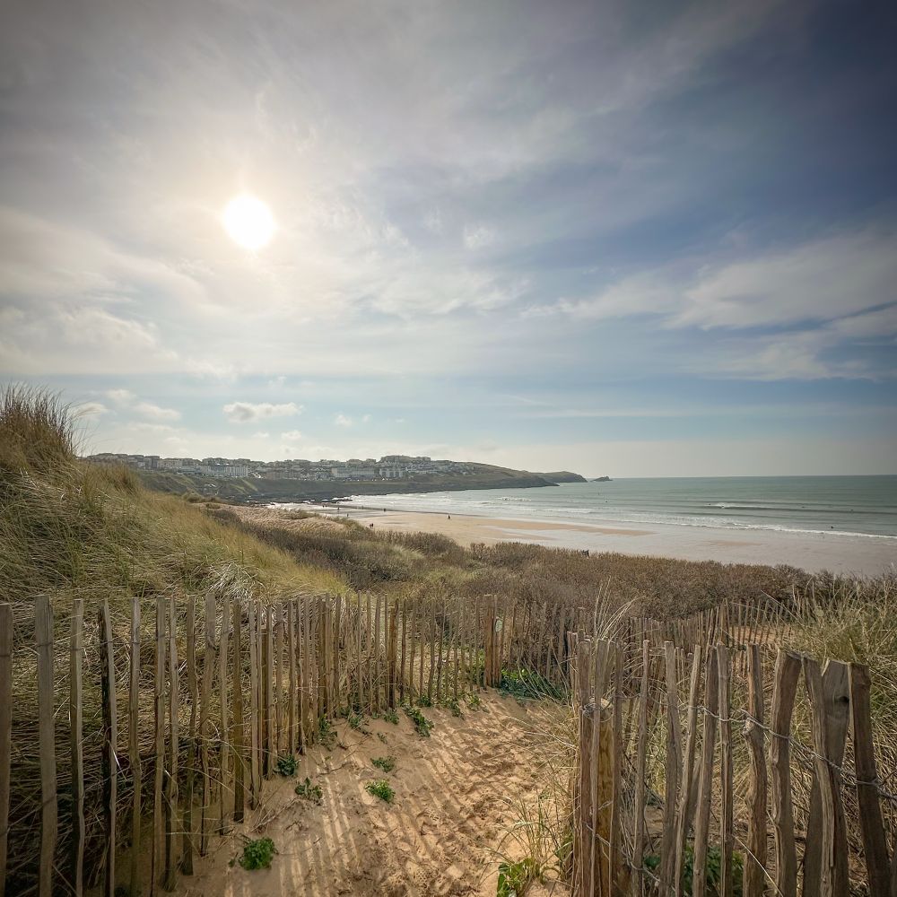 Photograph of the sandy path through the sand dunes to Fistral Beach in Newquay. The sun is out in a hazy march sky 