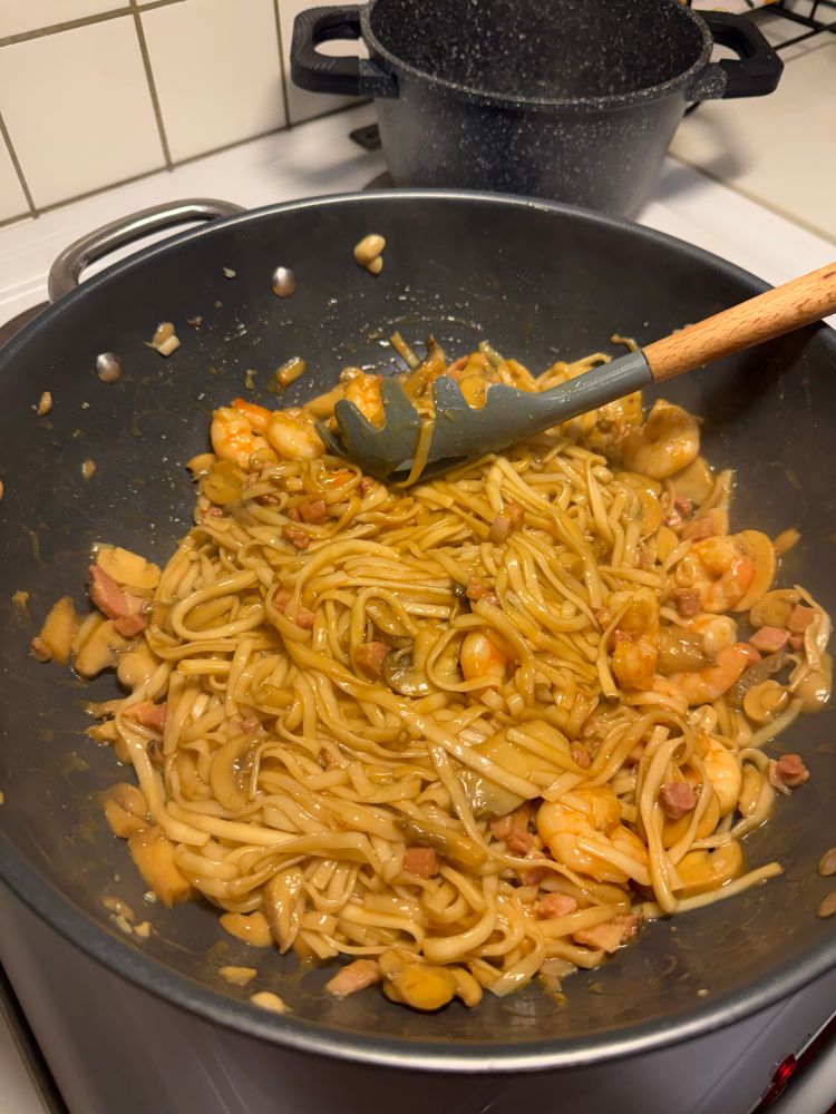 Udon noodles with king prawn and bacon in a wok pan