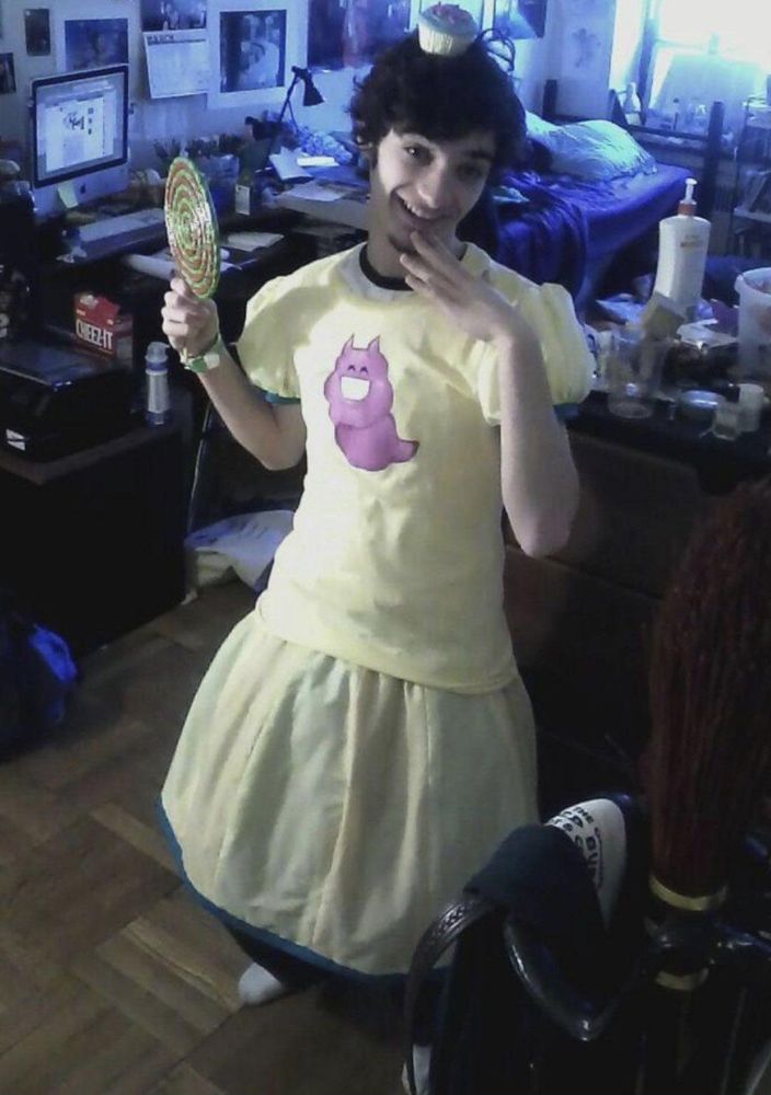 toby fox wearing trickster mode jane's outfit. he has a large bottle of lotion in the background.