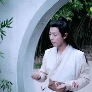 a man with long hair is standing in front of a white archway holding something in his hands .