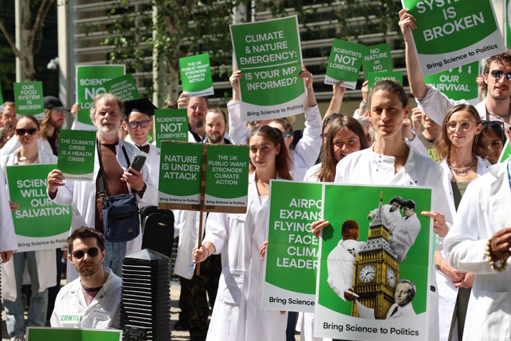 Scientists stand in front of DEFRA hold placards demanding political action to address multiple environmental crises. Image credit: Kirk Pritchard