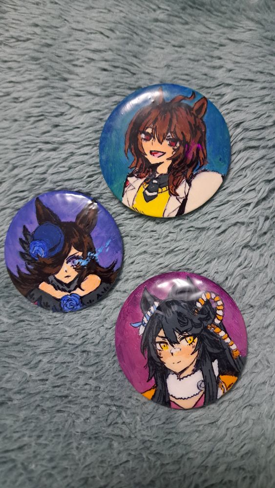 3 pins/buttons/can badges/whatever you call them. One has a portrait of Agnes Tachyon, one with Rice Shower and one with Narita Brian. (their Umamusume designs, not the real horses)