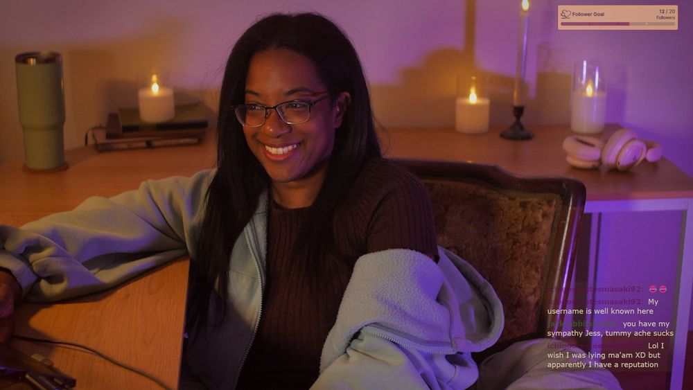 Jess wearing a brown dress and hoodie and giggling on stream