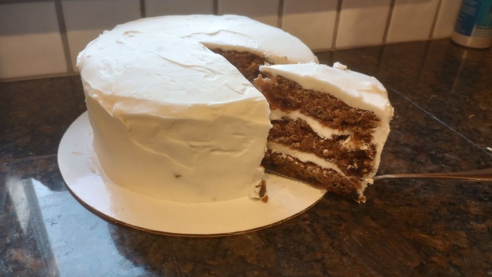 A photo of a three layer carrot cake with white cream cheese frosting.
