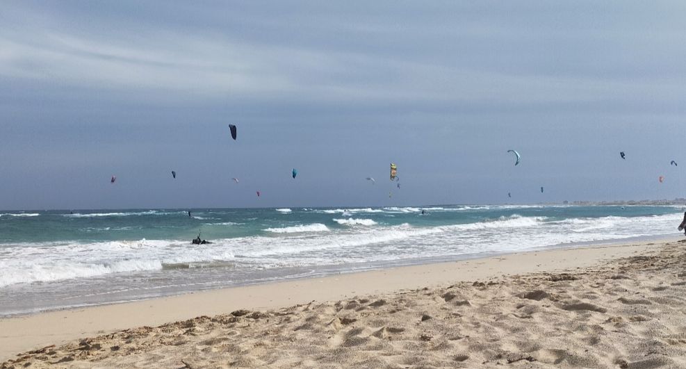 Sand, waves and a sky full of kitesurfing kites in all colours.
