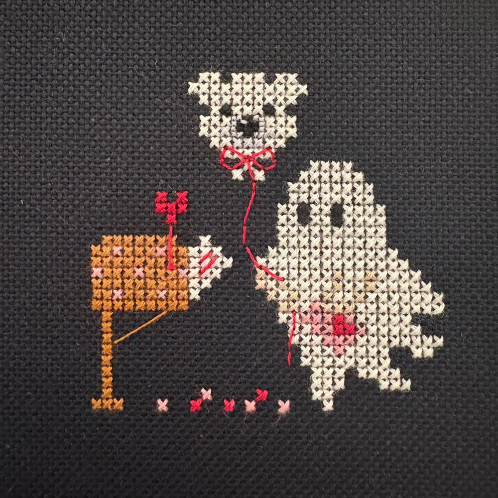 A small cross stitch design of a ghost in front of a mail box holding a teddy bear balloon.