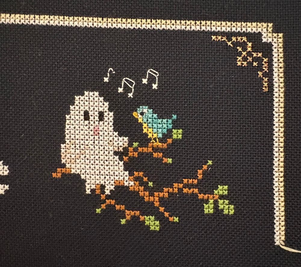 A cross stitch design featuring a ghost alongside a bird sitting on a branch.