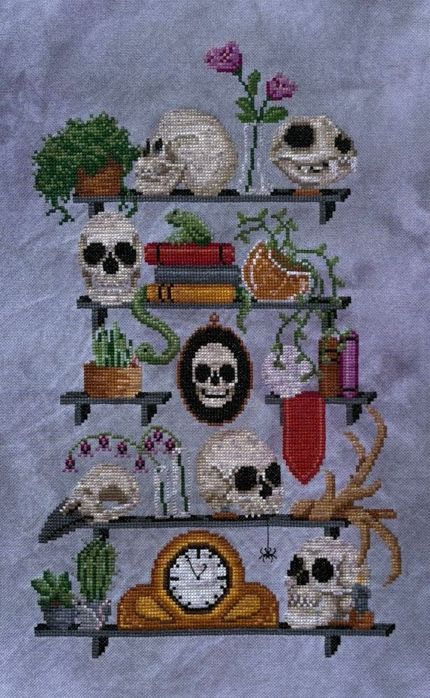 The cross stitch design A Study in Skulls stitched on purple fabric.