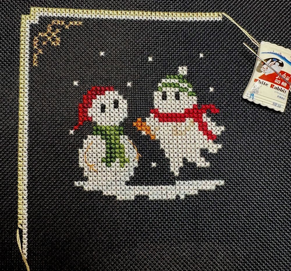 A portion of a cross stitch design featuring a ghost wearing a hat and scarf putting a carrot nose on a snowman.