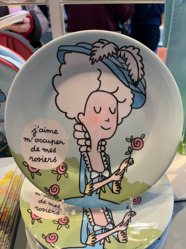 A plate featuring a cartoon version of Marie Antoinette with the words "j'aime m'occuper de mes rosiers".