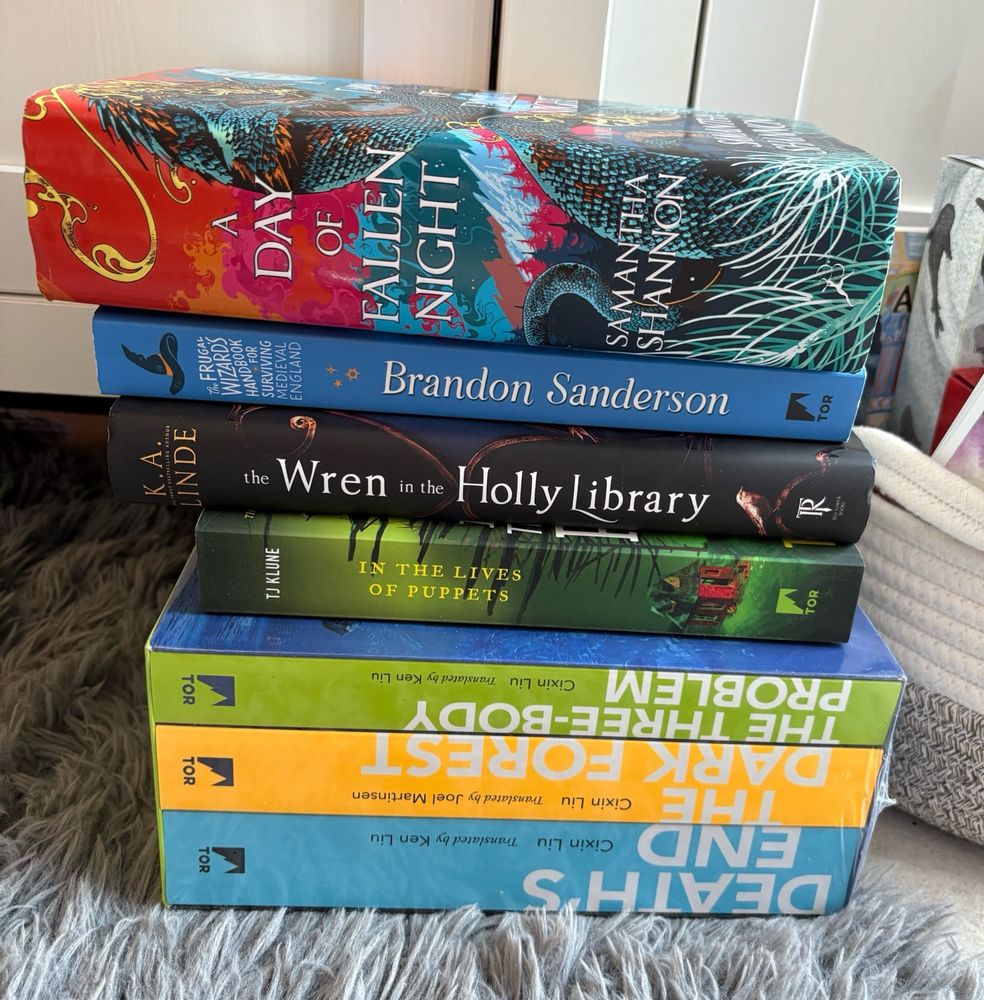 A pile of seven books sitting on a fuzzy grey rug. 
