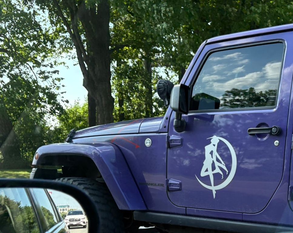 The front portion of a purple jeep-style car with a while Sailor Moon decal on the driver's door.