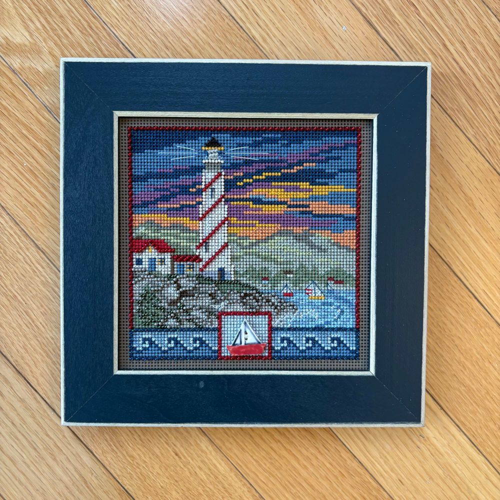 A framed cross stitch of Lighthouse by Mill Hill. 