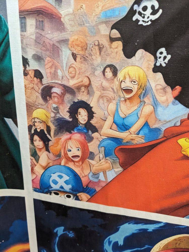 A close up of a one piece printed fabric visibly made by AI found in a fabric store in Paris in late 2024. Sanji is wearing a dress and his face seems to be melting. Brook gained human form again. Chopper looks human as well but seems to now have strabismus. Law shaved his beard and bleached his hair.