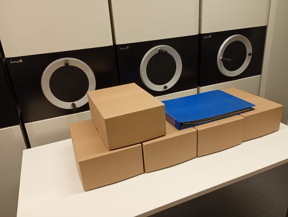 Five boxes and a photo album on a table in an archive store with moveable shelving. 