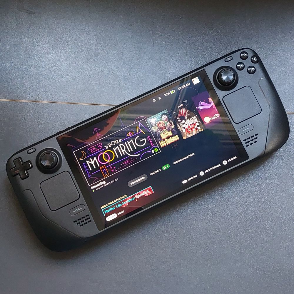 Photo d'un Steam Deck OLED posé sur un bureau noir. Sur le menu, on voit les jeux Moonring, Muffles Life Sentence, Nightmare Kart et OneShot.