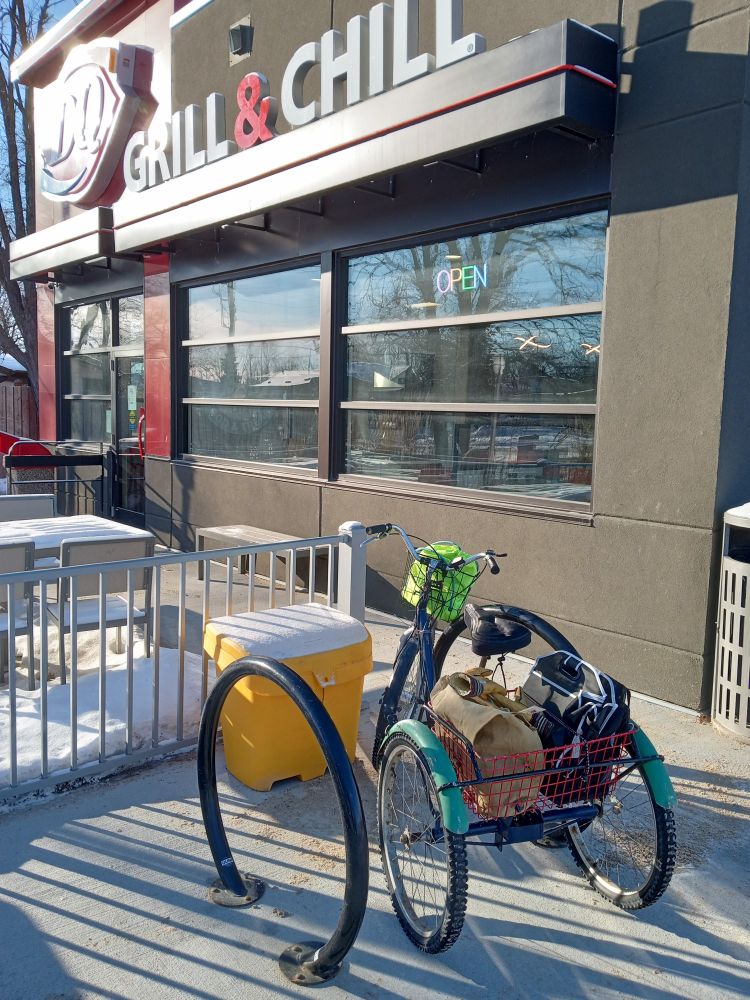 Blue trike with bright green fenders parked at bike rack at DQ. Snow has been cleared around bike rack!