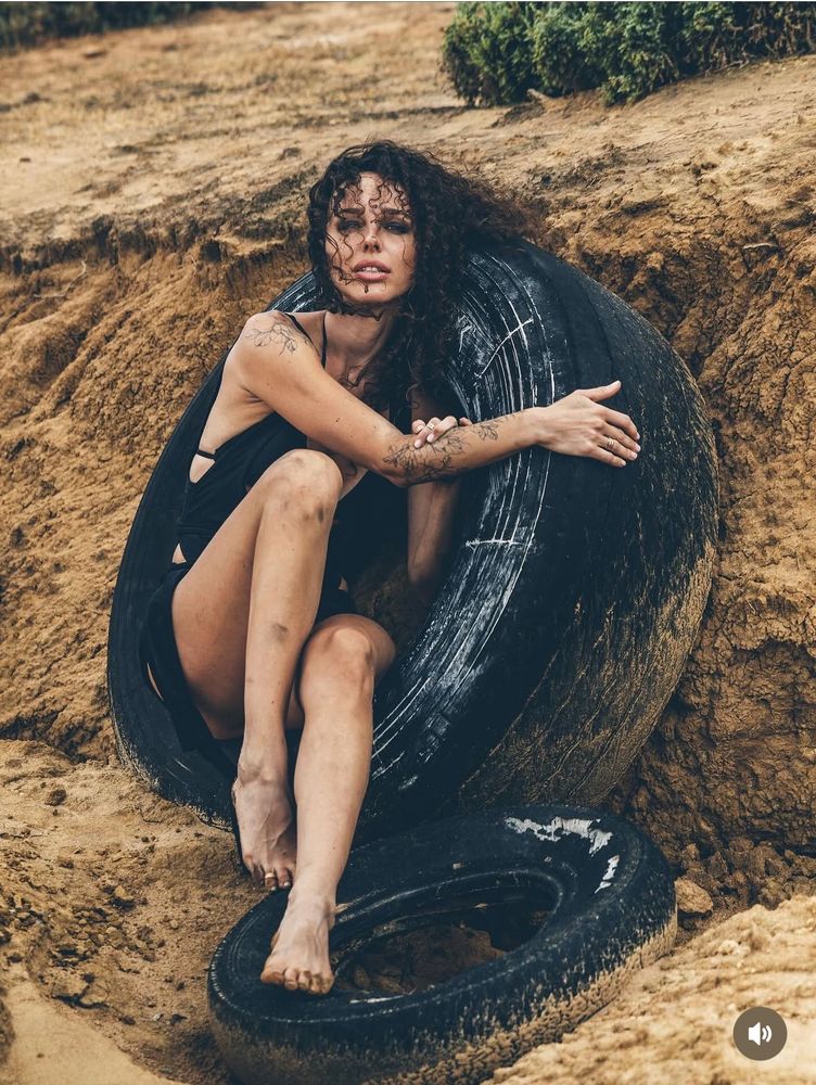 Portrait of a dark haired Ukrainian woman looking disheveled in a little black dress seated within a truck tyre 