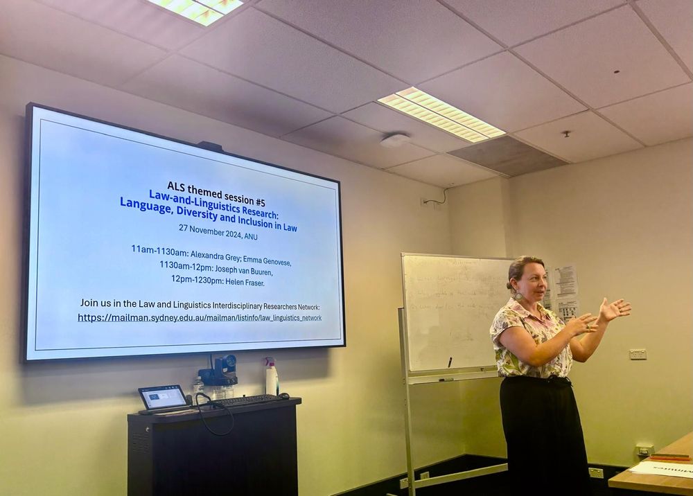 Woman stands at the front of a classroom, in front of a screen with a slide showing ALS themed session "Law-and-Linguistics research: language, diversity and inclusion in law"