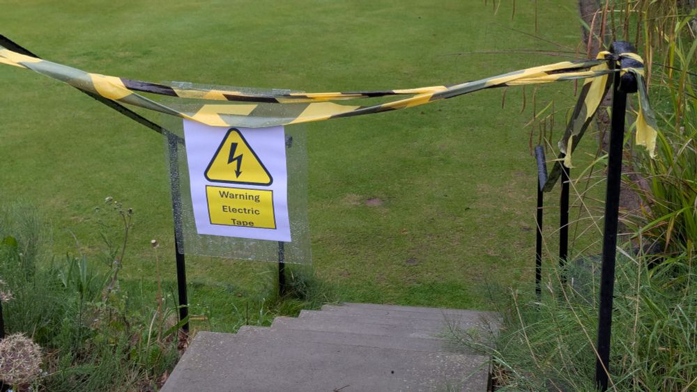 Sign showing 'Warning Electric Tape' on entrance to bowling green
