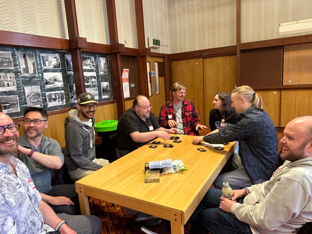 8 of this week's attendees sitting around the table playing Uno No Mercy. Lots of laughter, someone picking up a lot of cards, and of course everyone is looking in random directions and about 3 different conversations are going on.