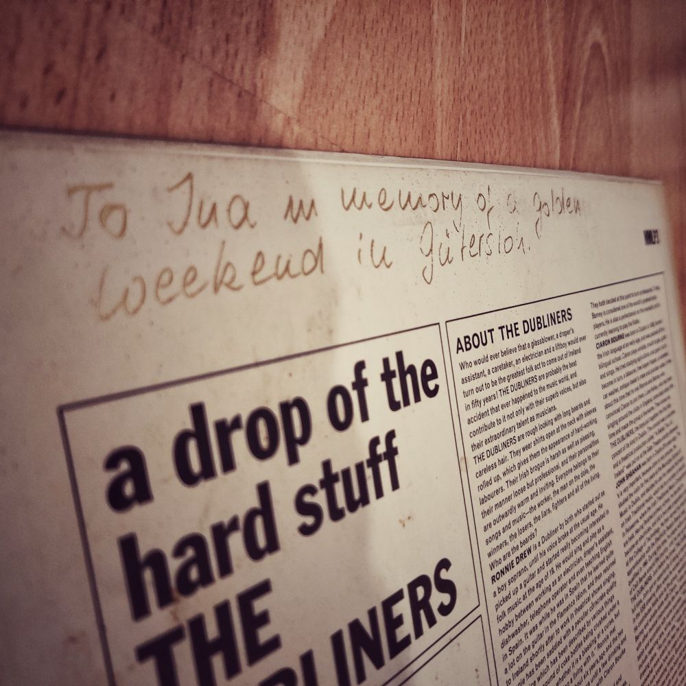 Close-up of the backside of a record sleeve. The album in question is A Drop of the Hard Stuff by the Dubliners.
A note has been written on it in gold ink. It says: "To Ina in memory of a golden weekend in Gütersloh."