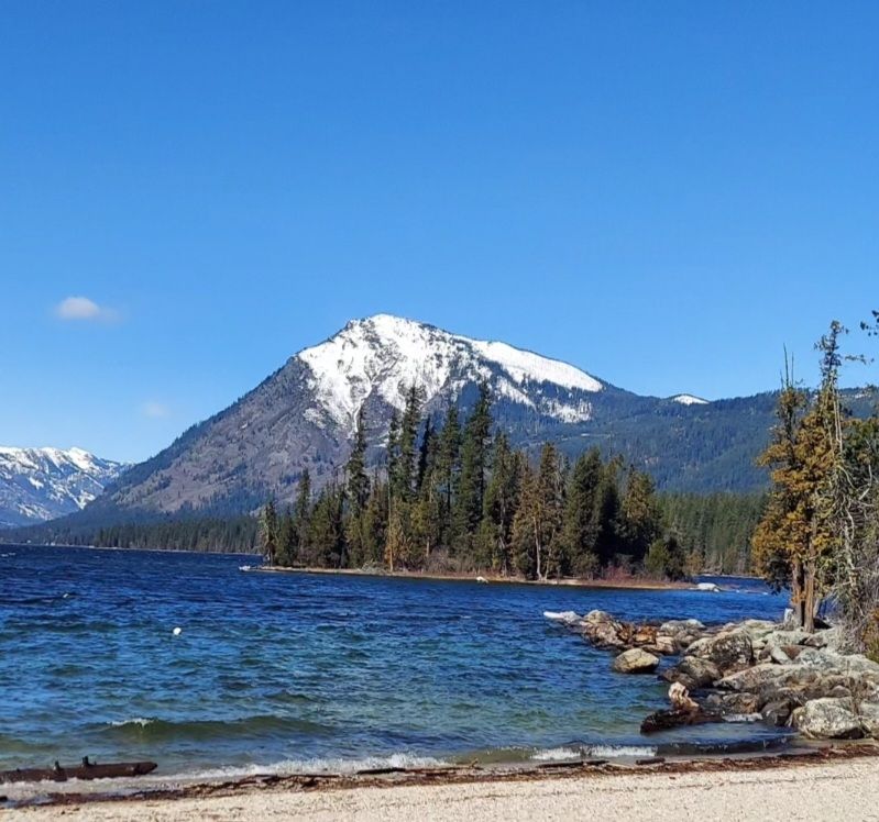 Snow capped mountain under blue sky beside a blue lake.