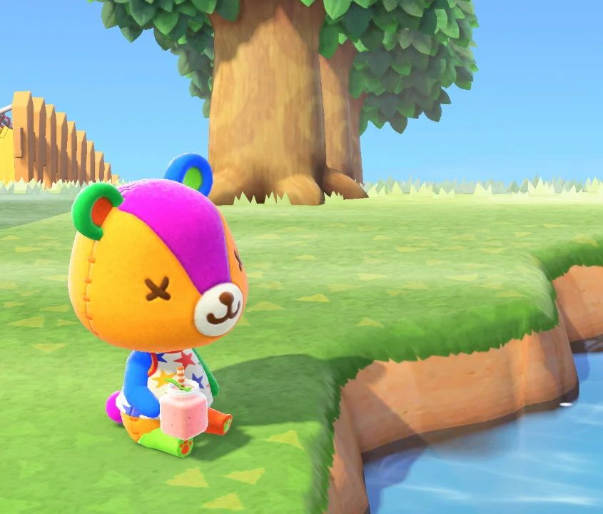 Stitches from Aninal Crissing sitting on the grass with a smoothie. It’s a colourful teddy bear.
