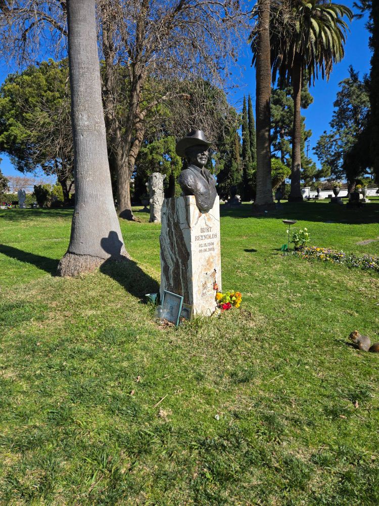 Burt Reynolds' grave with a tree in the background. Behind that tree is a squirrel with a can of Red Bull. 