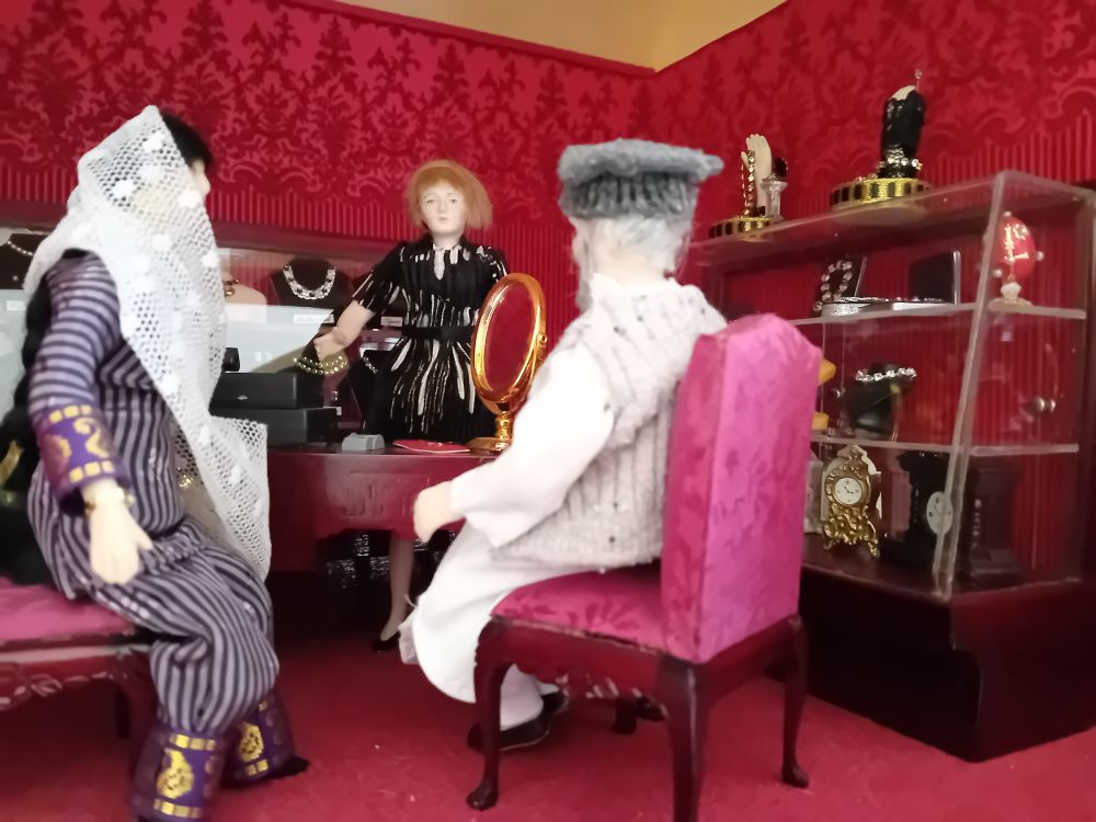 A dollshouse scene - a Muslim dad buys his daughter jewellery in a shop.