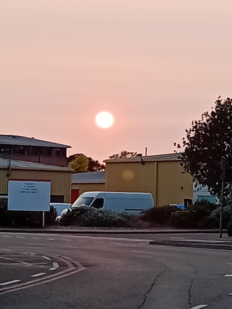 Lage setting sun in a pink sky over industrial units and white vans.