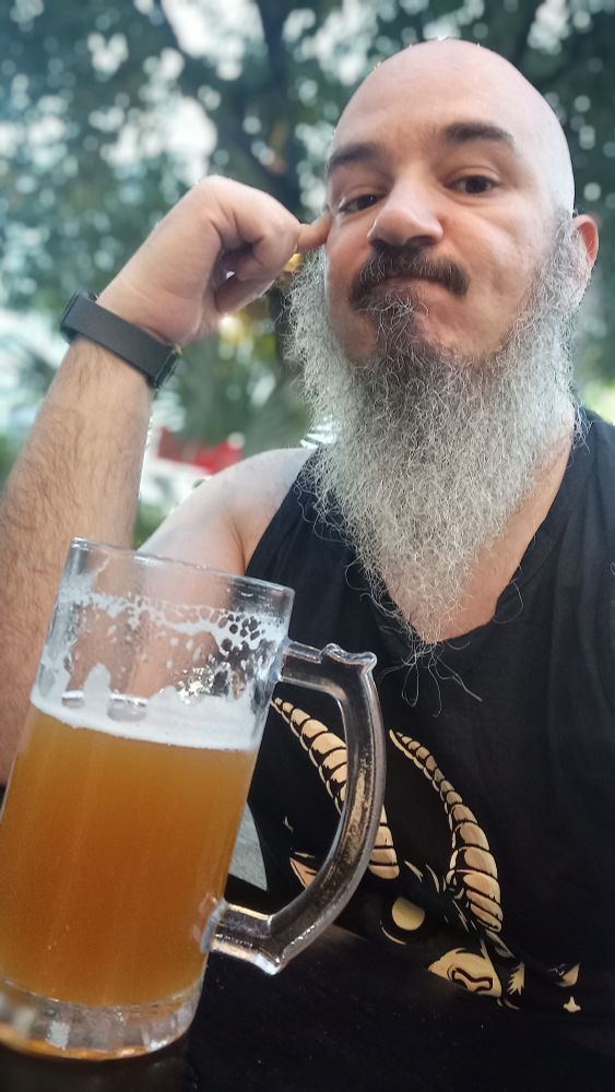 Homem careca, barba branca, camisa preta sem manga com caneca de chopp na frente.