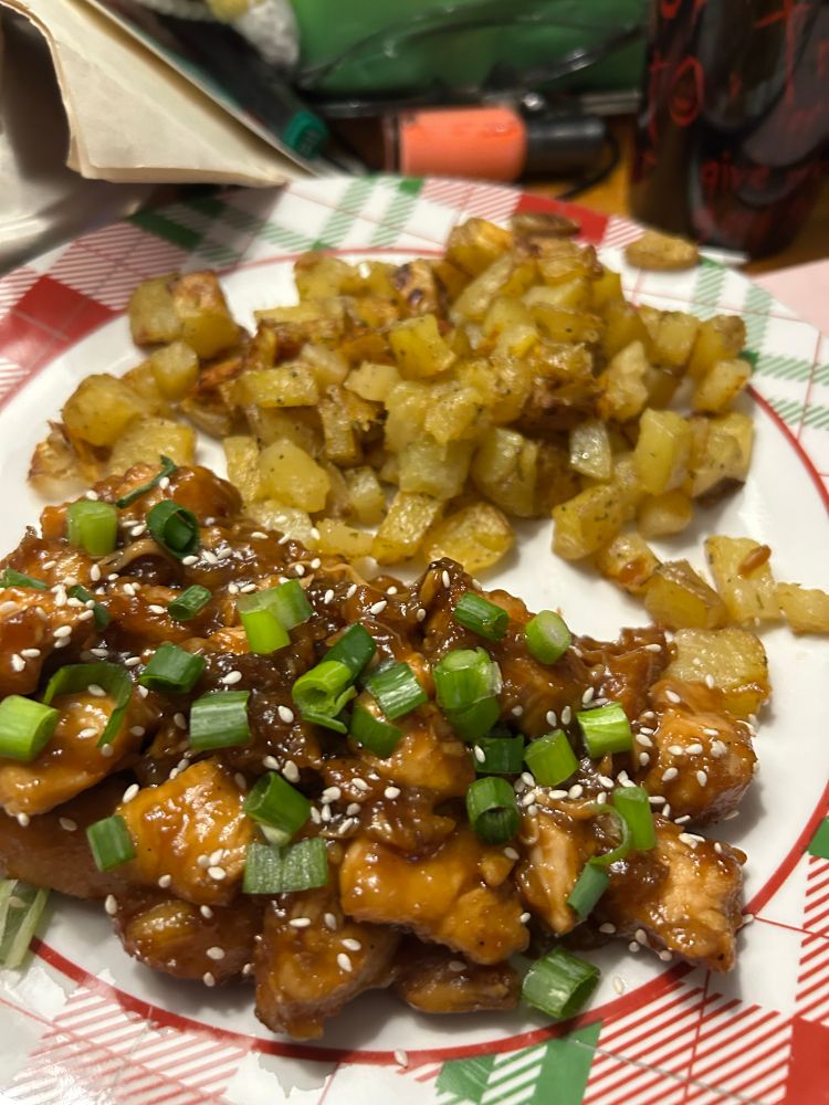 a plate with saucy chicken with green onions and sesame seeds and cubed roasted potatoes 