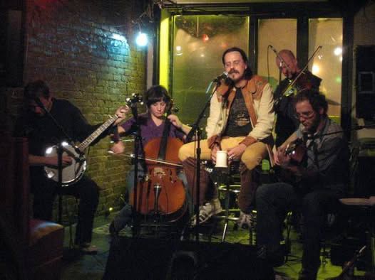 me sitting on a stage in a window of a bar playing music with my bandmates. i'm flanked by a banjo, fiddle , cello and guitar.