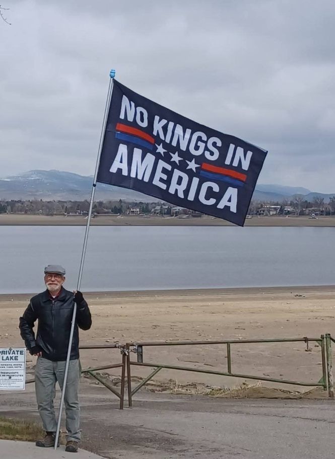 Man holding no Kings in America flag next to a lake.