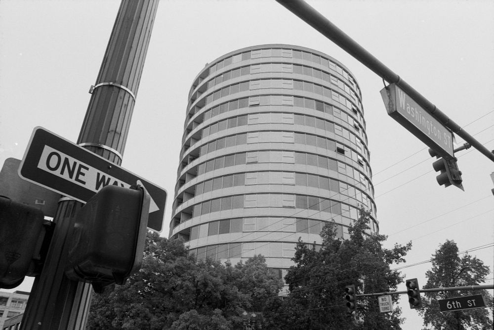 Cylindrical building behind trees, traffic signs and traffic light 