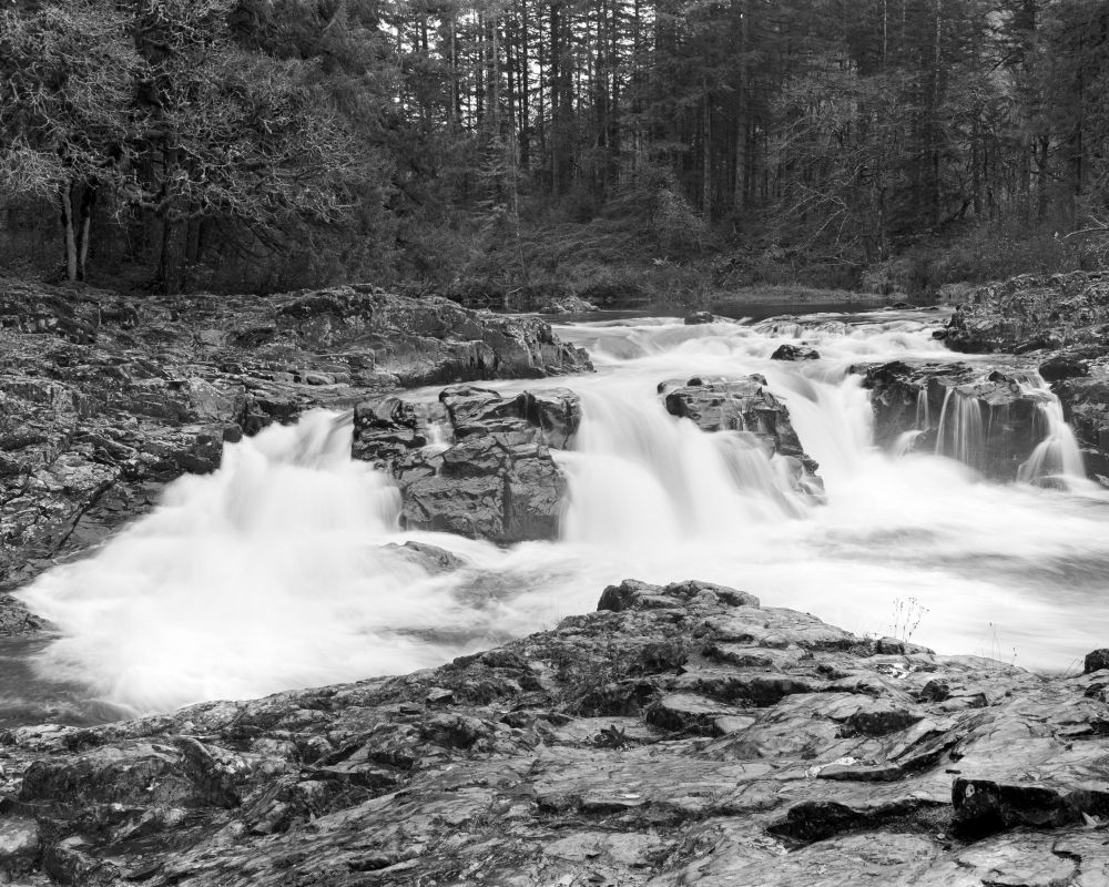 Small waterfall split into three by rocks framed by rocks with a backdrop of trees