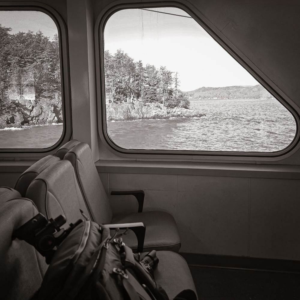 View of the edge of Lopez Island from inside the ferry framed by a window with seats and backpack in foreground