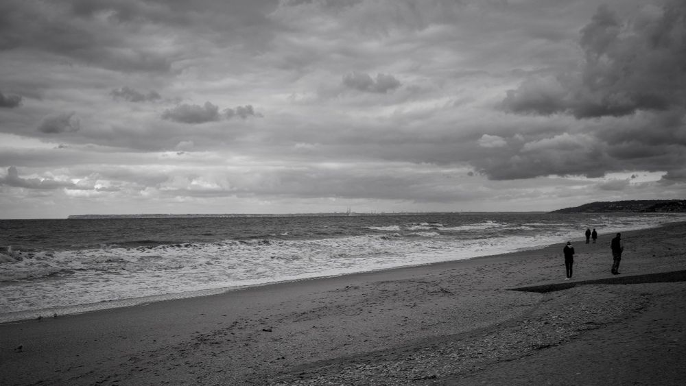Two couple on a beach, one couple bookend the other. Fresh wind drives the waves below and the clouds above. 