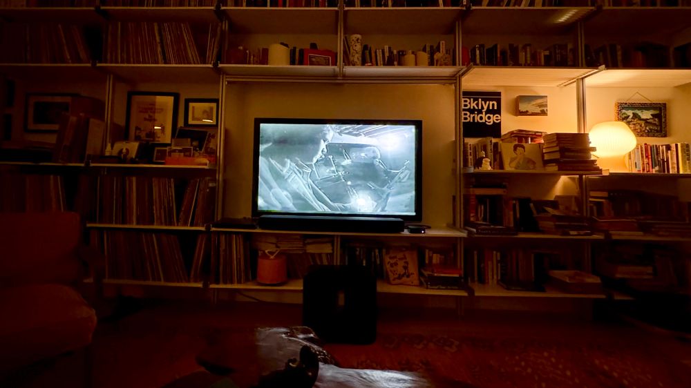 A tv in the center of a wall - it’s surrounded by books and LPs. On the screen is the music video Precision Auto by Superchunk.
